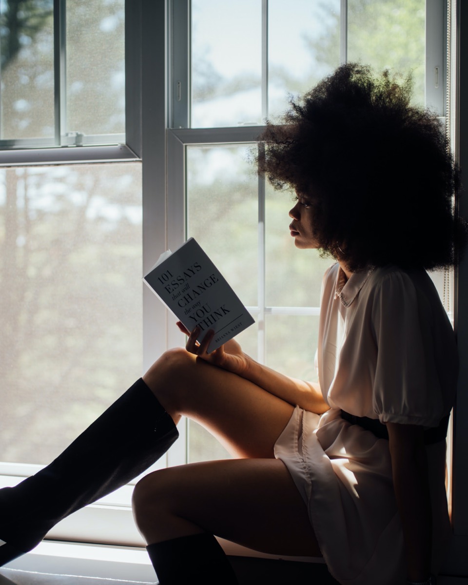 A Black woman with natural hair reading by a sunlit window