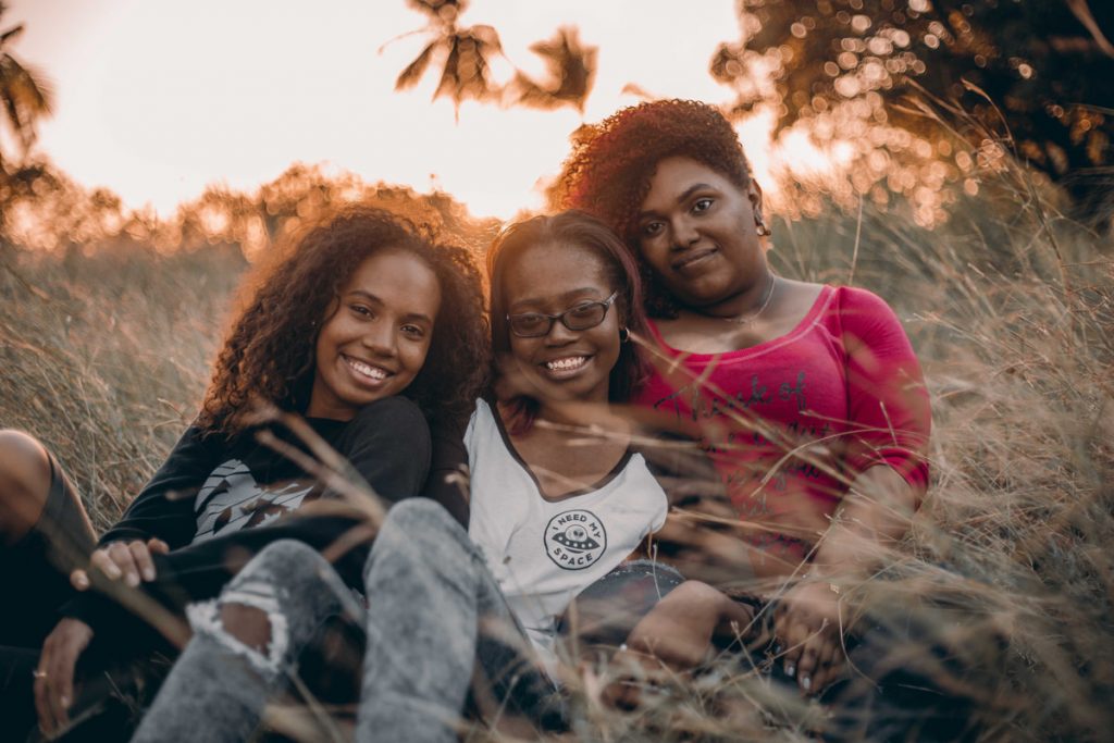 Three young women sitting close together in tall grass, smiling