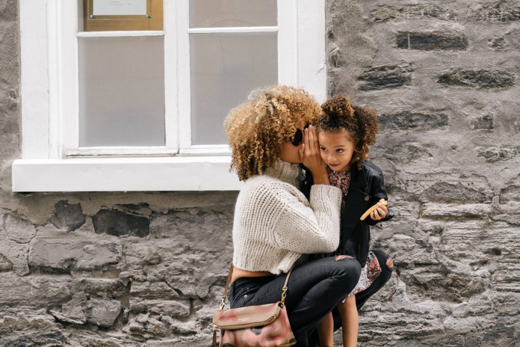 A parent crouching to whisper to a young child